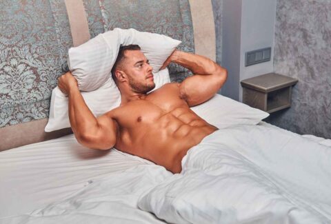 shirtless-sexy-muscular-male-model-lying-alone-his-bed-his-bedroom-looking-away_11zon