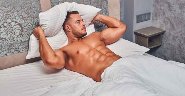 shirtless-sexy-muscular-male-model-lying-alone-his-bed-his-bedroom-looking-away_11zon